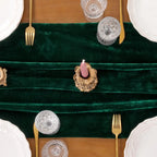 Chemin de table en velours vert vu de dessus avec assiettes et couverts dorés